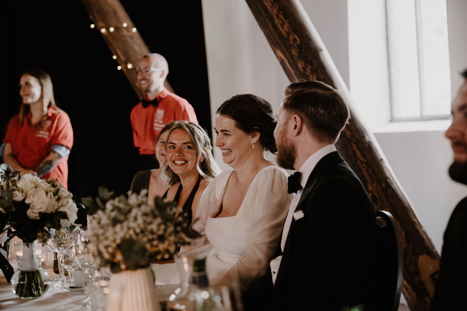 Wedding reception candid photo showing guests enjoying dinner at elegantly decorated tables in a bright venue.