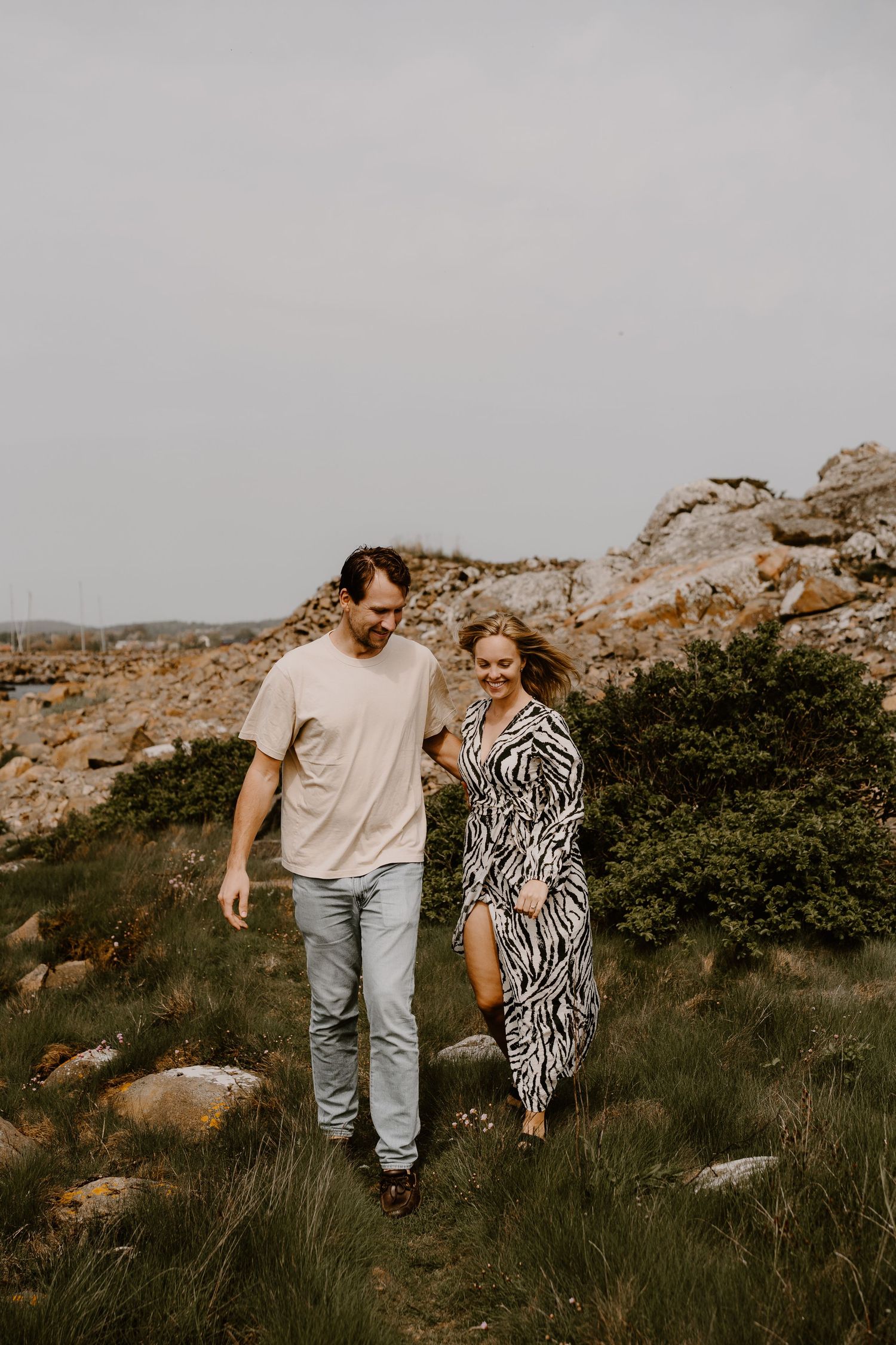Couple walking together on a rugged hillside with rocky terrain and green brush on an overcast day.