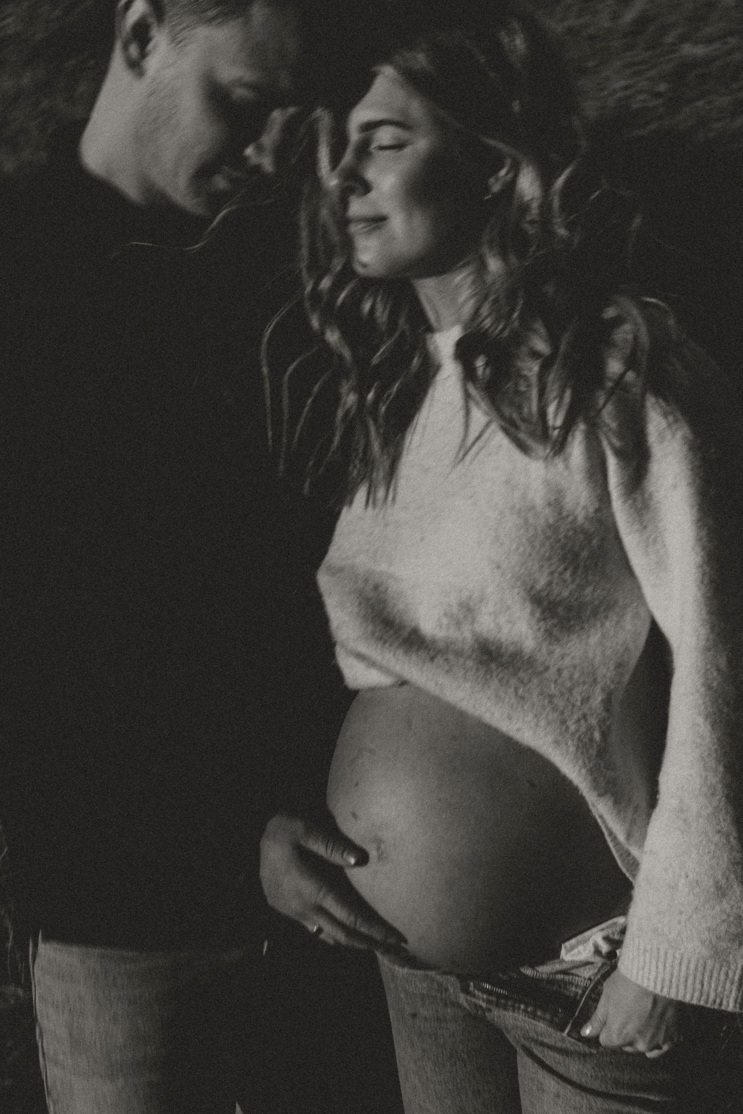 An intimate black and white maternity photo captures a tender moment between expectant parents.