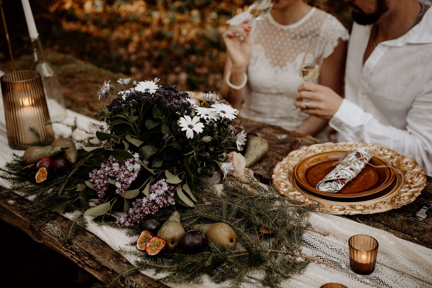 Elegant table setting with moody floral centerpiece, candles, and decorative plates at rustic outdoor reception dinner.