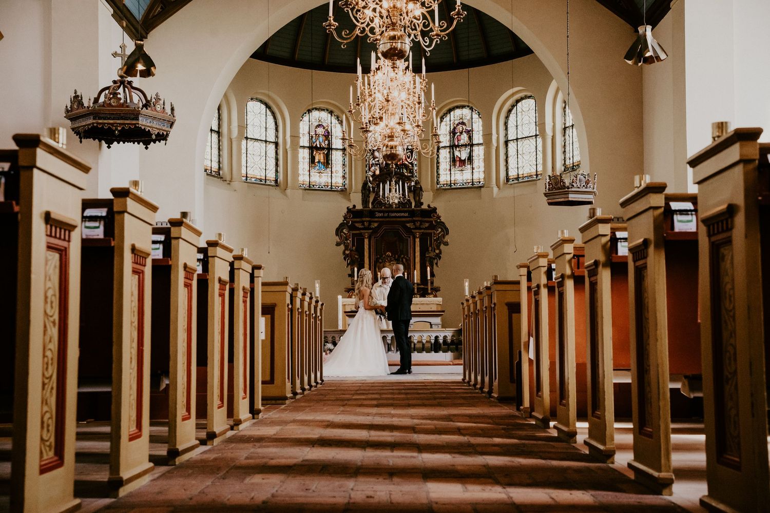 Classic church interior with wooden pews, soaring arches and chandeliers creates dramatic aisle framing a distant altar.