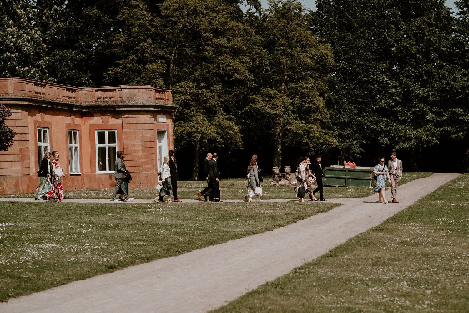 Students walk along a winding path near a historic brick building on a sunny day at a university campus.