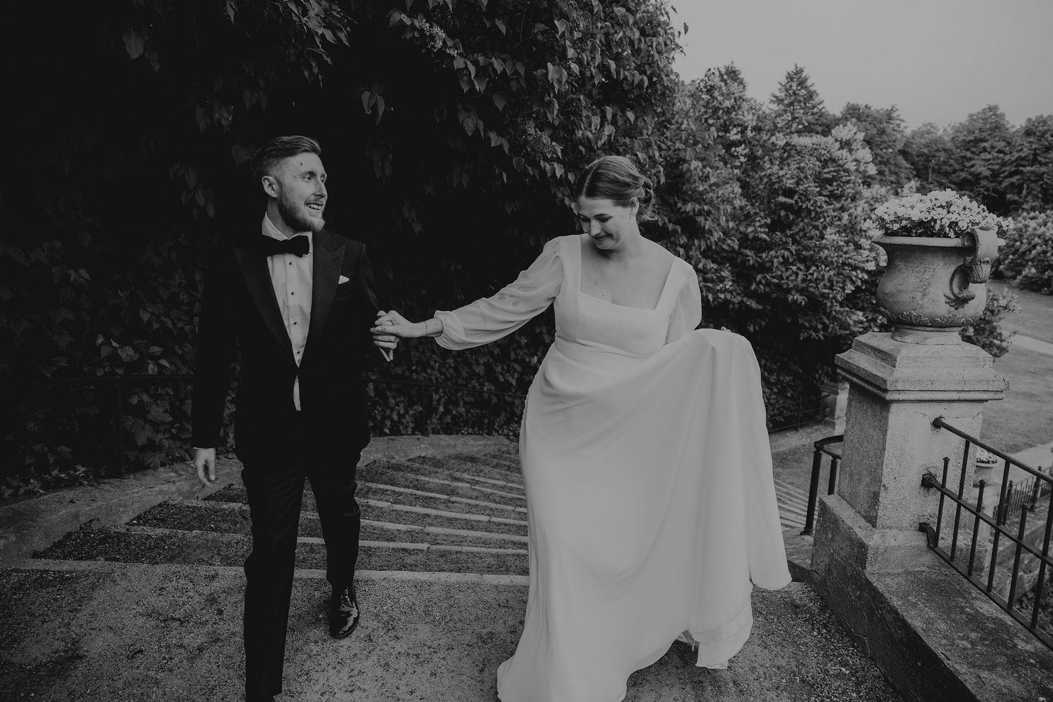 A romantic black and white panorama of newlyweds walking together through outdoor locations during their wedding photoshoot.