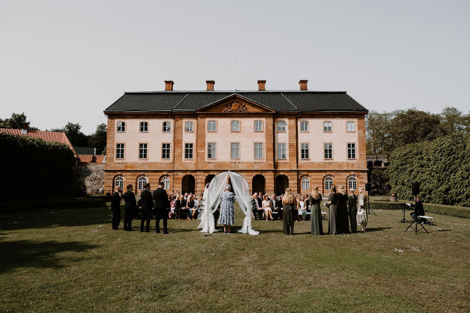 A panoramic sequence of wedding photos showing a grand brick mansion venue and guests gathered on a lush green lawn.