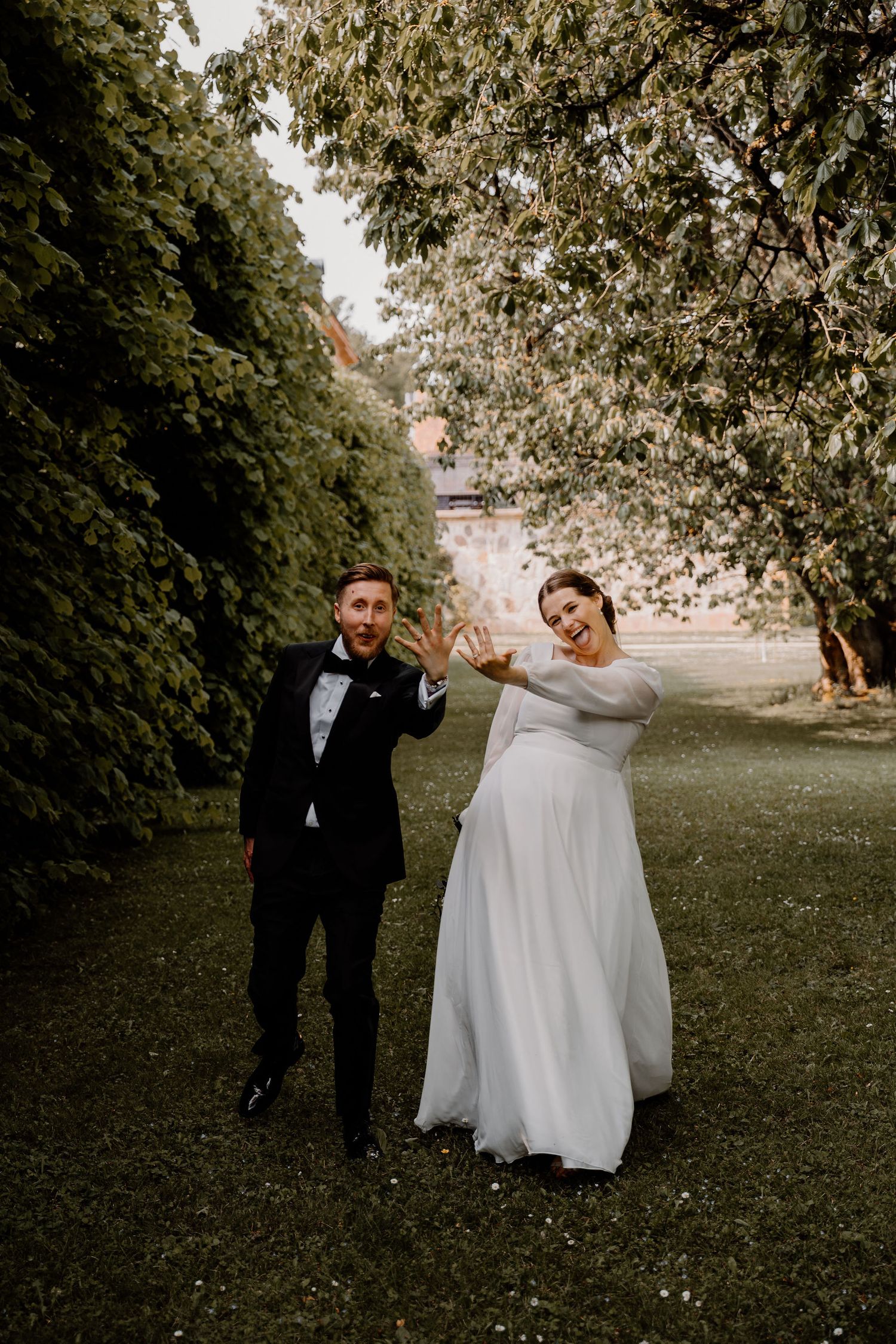 A fun wedding couple strikes playful poses in a lush green garden setting during their portrait session.