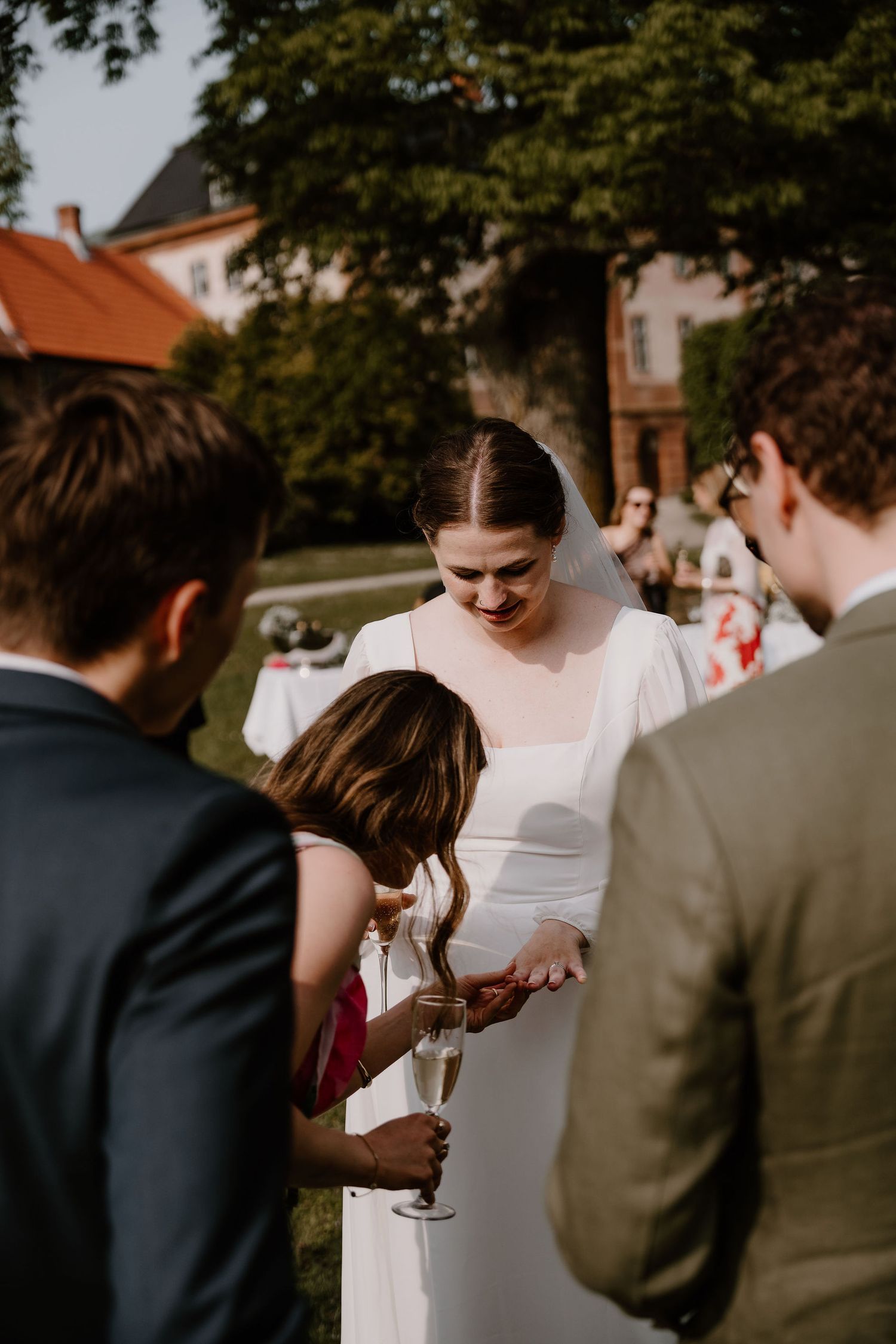 A bride in a white dress shares a laugh with wedding guests during an outdoor garden reception.