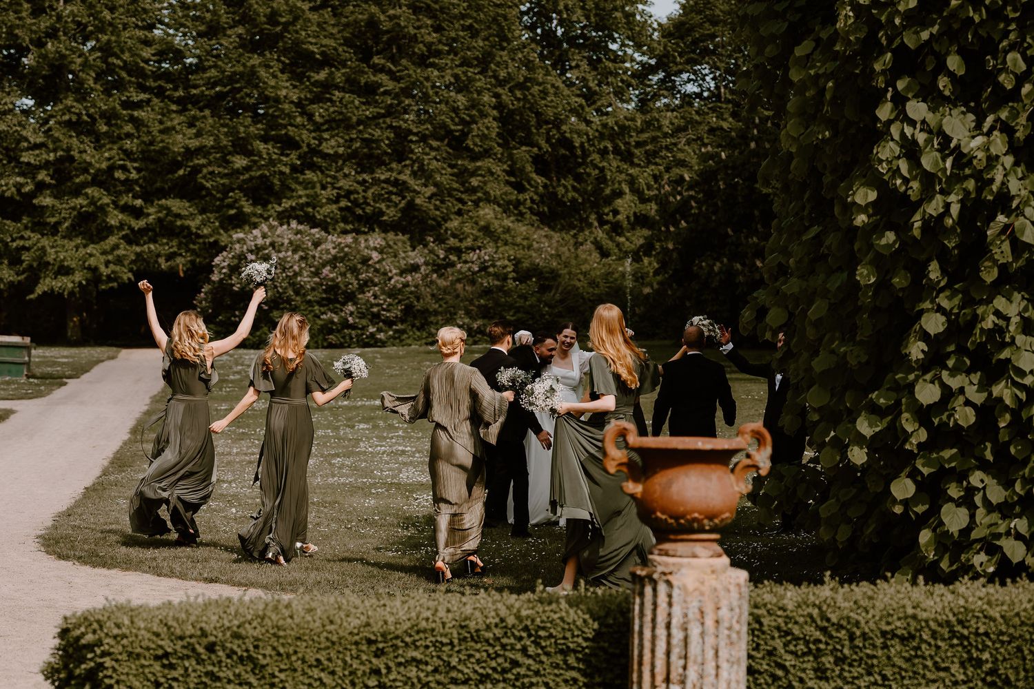 Guests enjoying an outdoor celebration with arms raised in joy on a grassy lawn near trees.