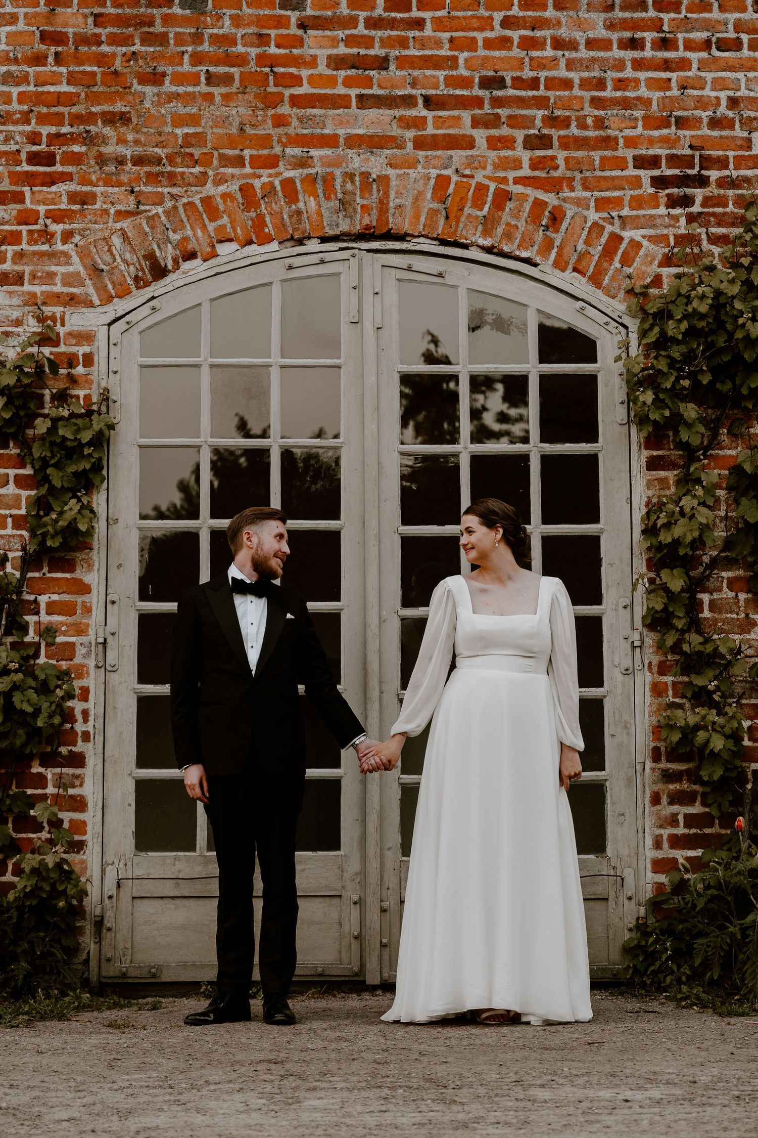 Wedding couple shares romantic moments in front of a rustic brick wall with elegant white French doors.