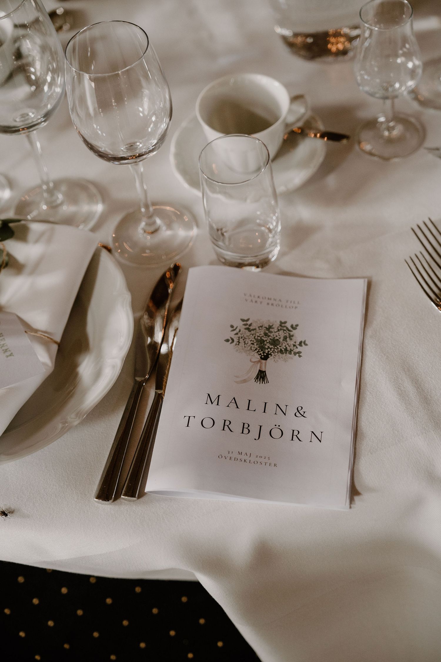 Elegant place settings at a wedding reception featuring name cards and white tablecloths with wine glasses and cutlery.