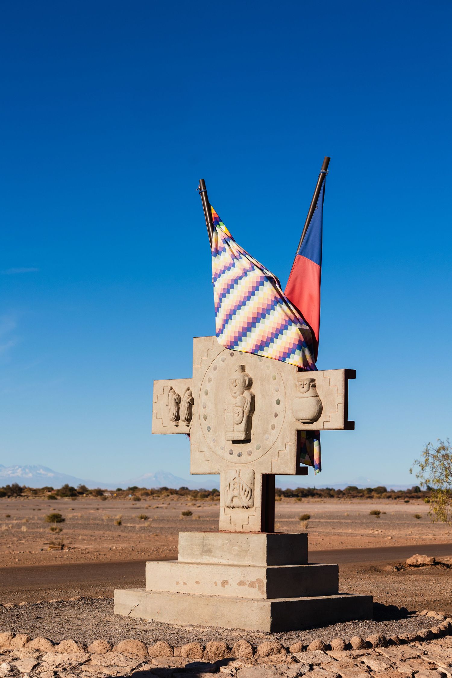 A desert monument made of concrete with red and blue stripes stands against a bright blue sky in multiple viewpoints.