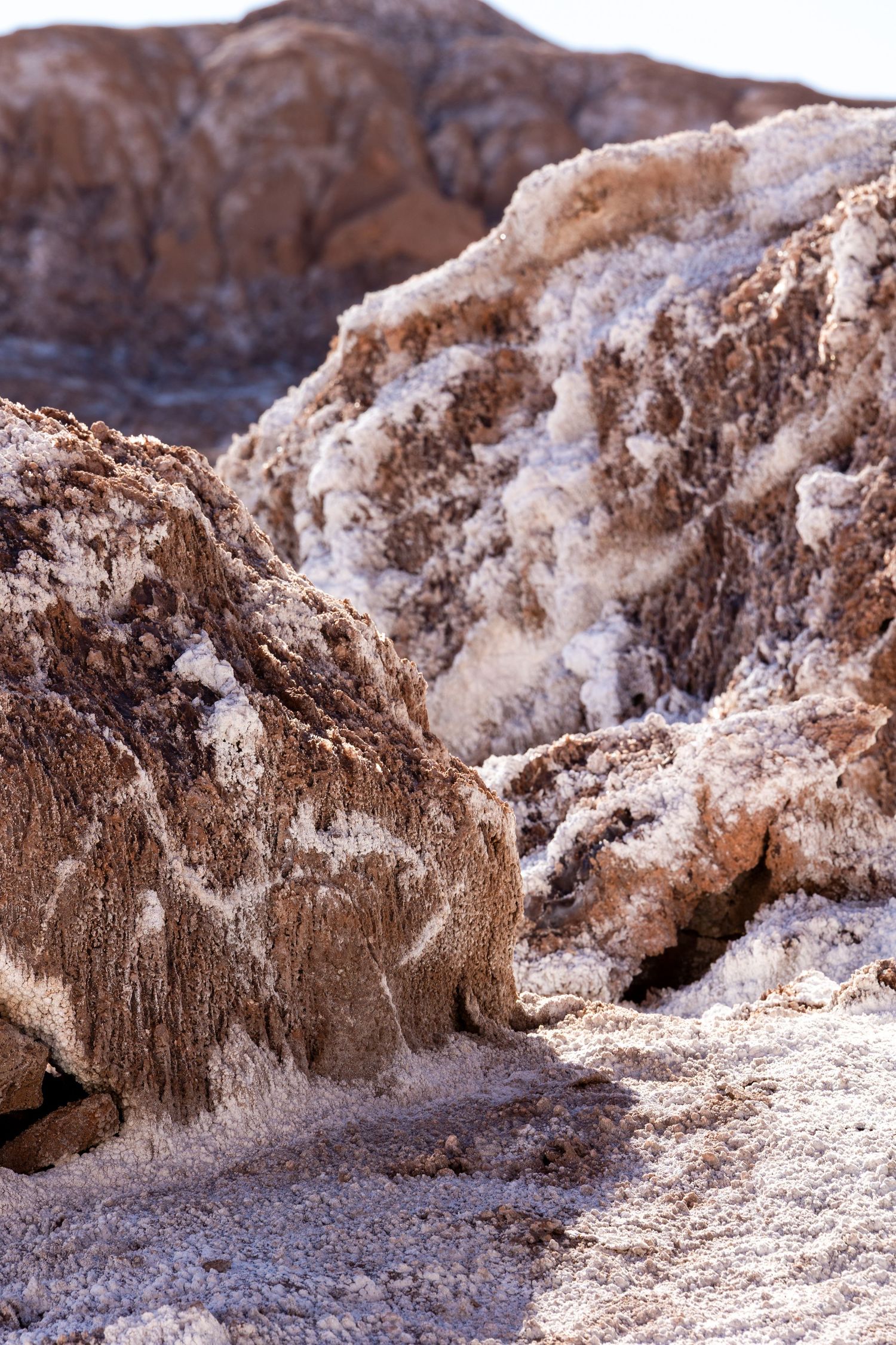 Salt formations and mineral deposits cover rocky terrain in an arid desert landscape.