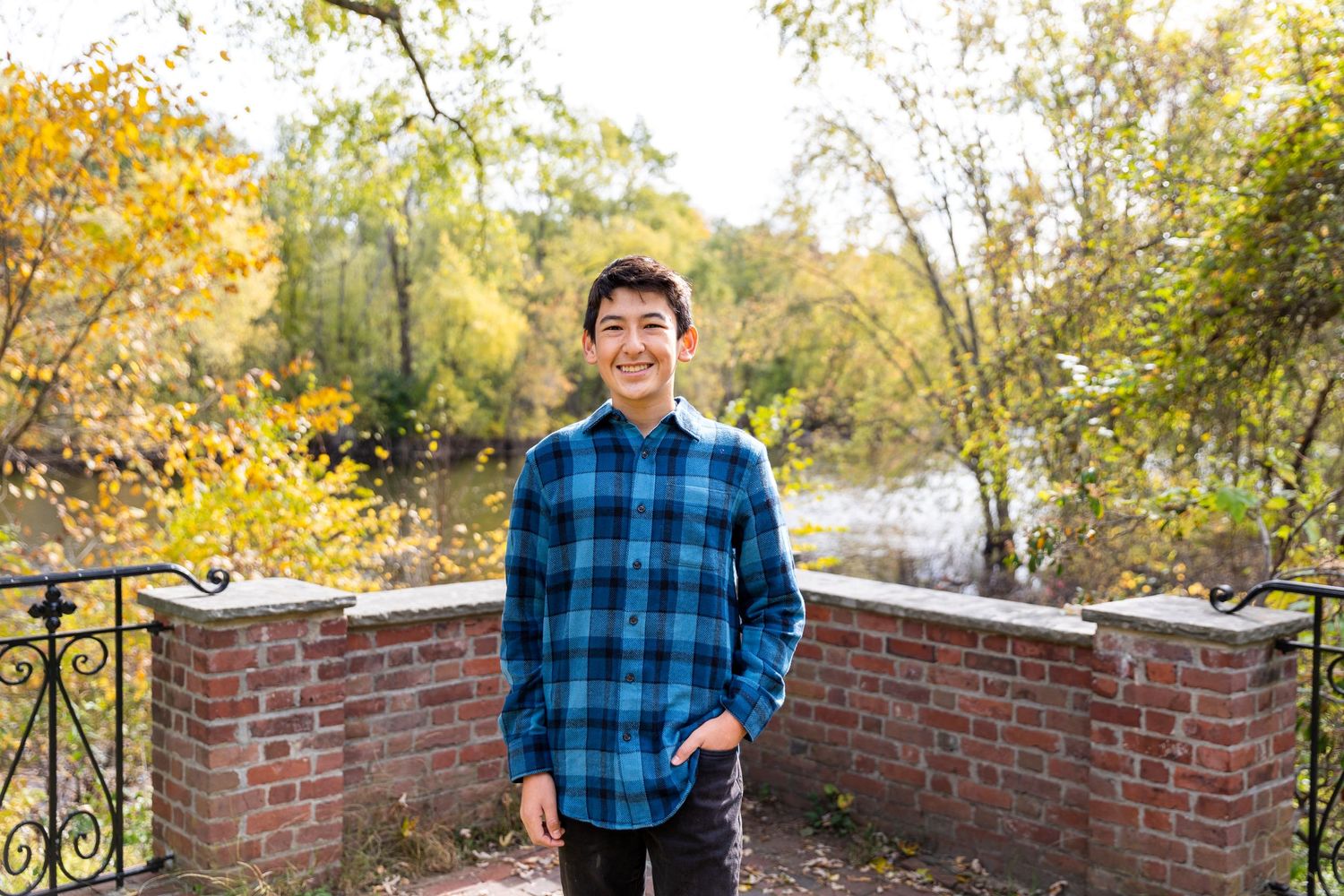 A person in plaid shirt stands by brick wall during autumn season.