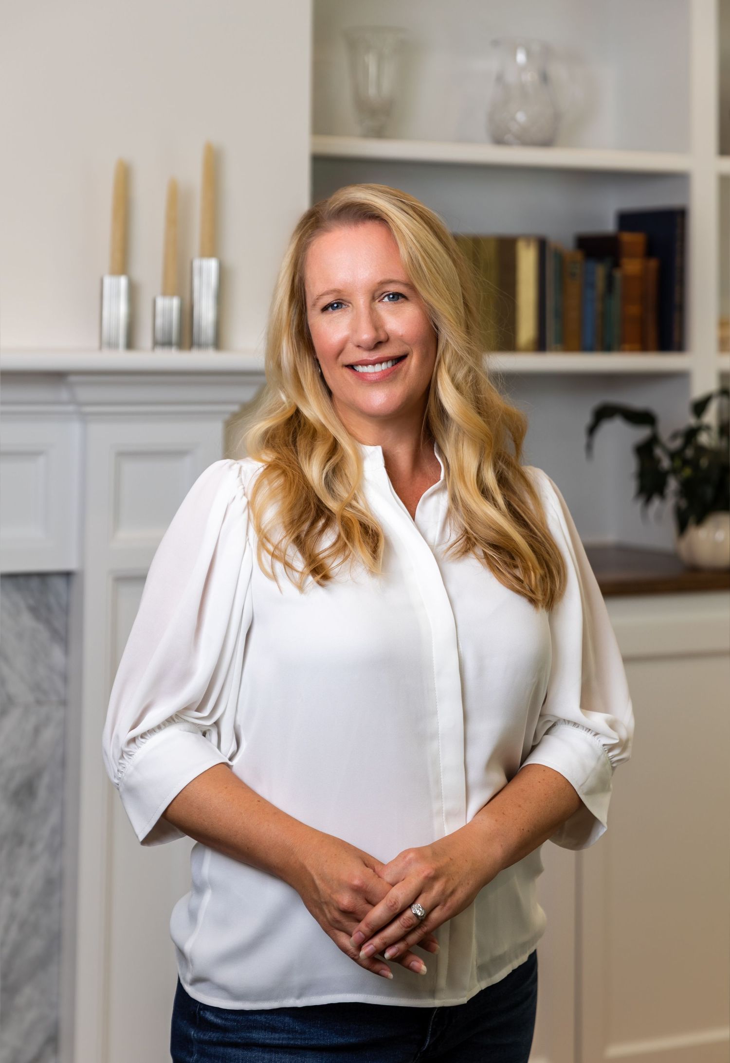 Professional business portrait of a welcoming presence in a white blouse against a bright modern kitchen background.