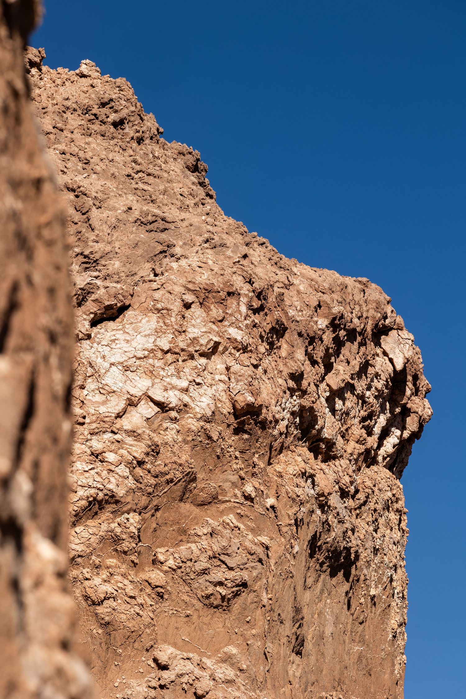 Close-up view of a rugged desert rock formation with brown tones against a bright blue sky.