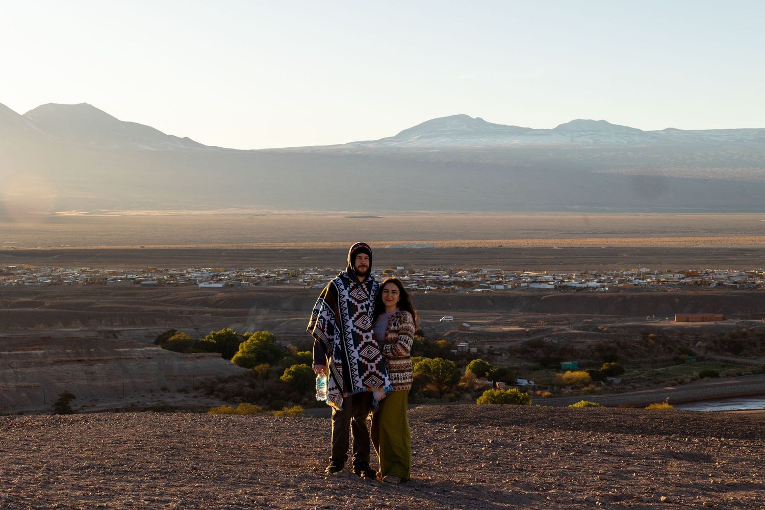 Arid desert landscape with distant mountains and desert scrublands under an expansive cloudy sky.
