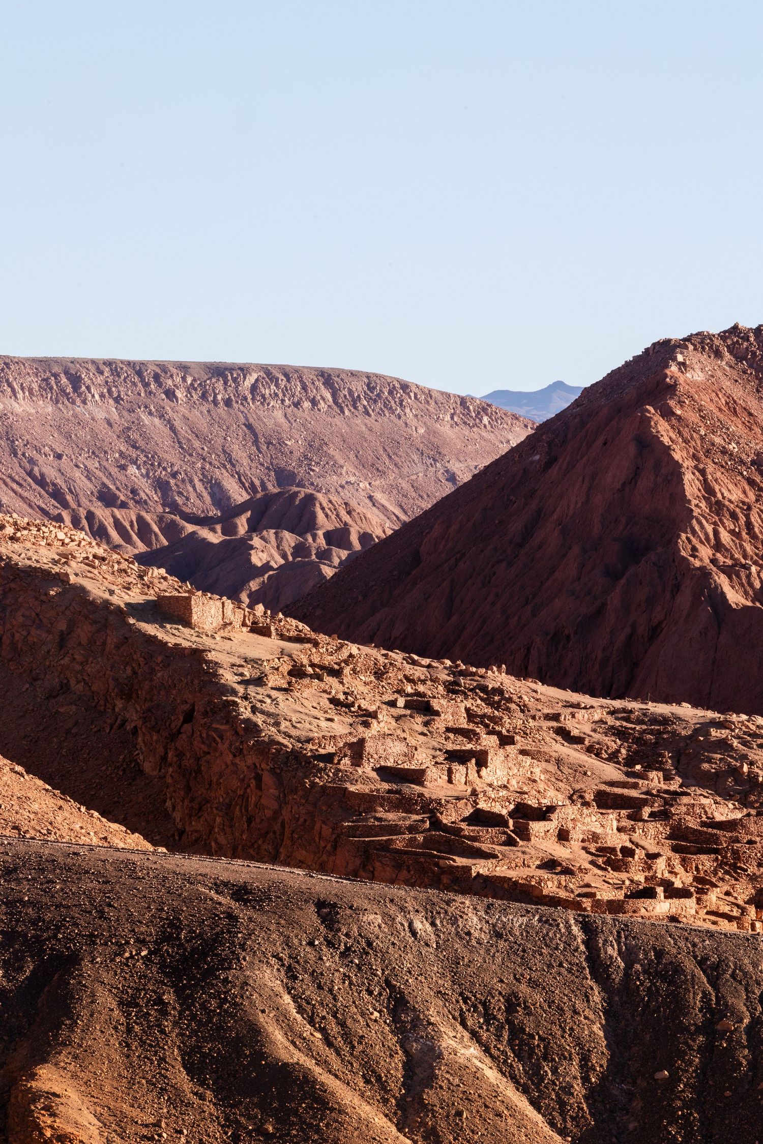 Ancient mud-brick buildings nestled within dramatic mountain peaks of the Moroccan Atlas Mountains at sunset.