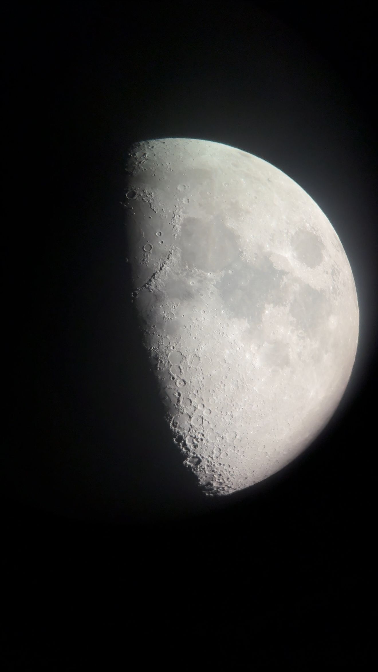 A detailed view of the moon in its first quarter phase showing craters and surface features against a dark night sky.