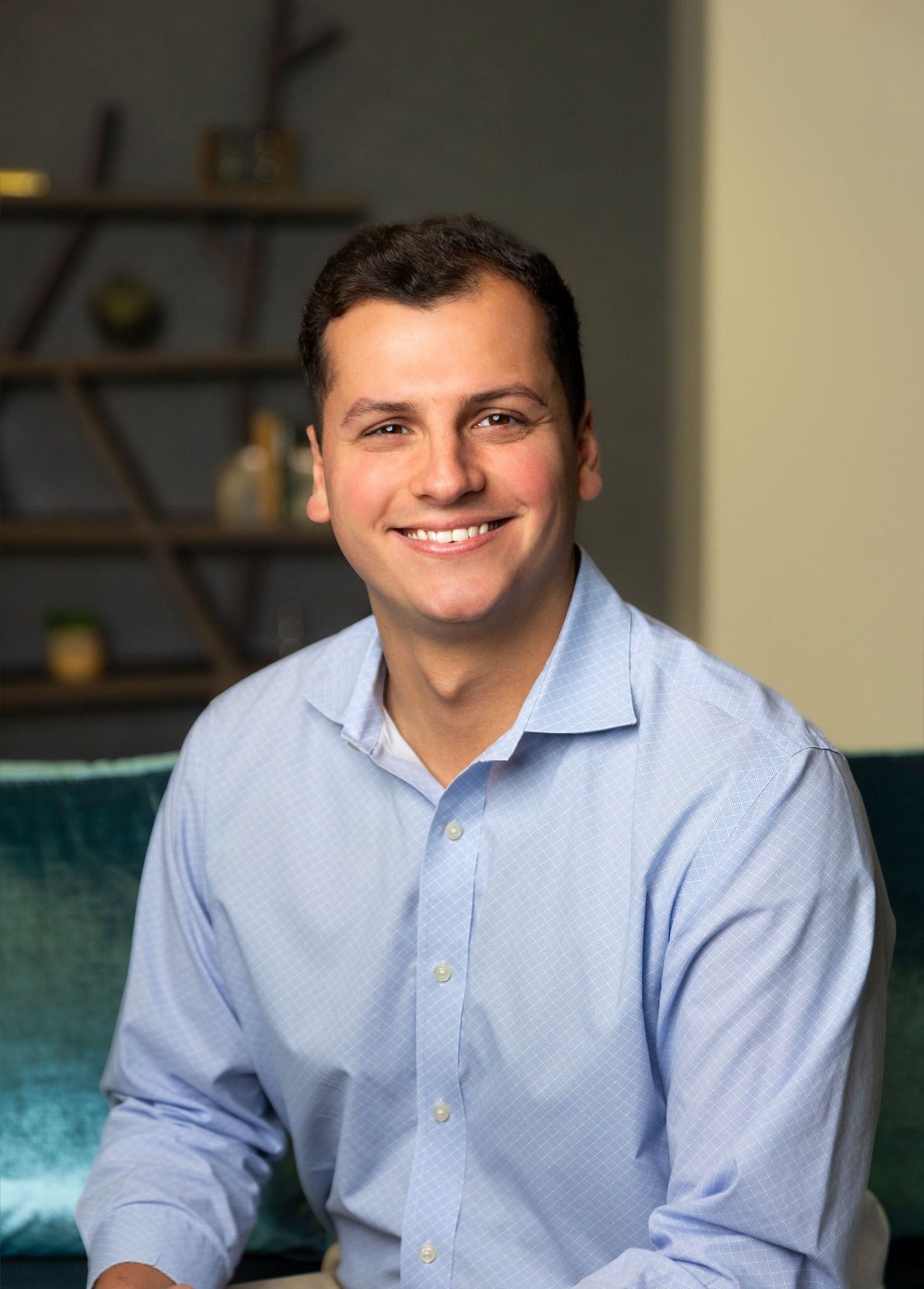 Professional in light blue button-down shirt smiles while seated on teal couch.