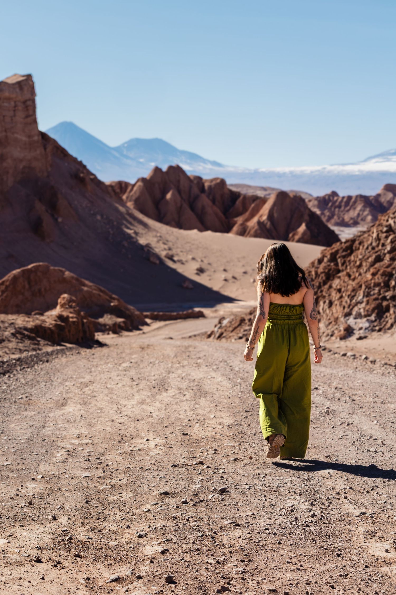 A wanderer in a flowing green dress explores the rugged terrain of Valle de la Luna in Chile's Atacama Desert.