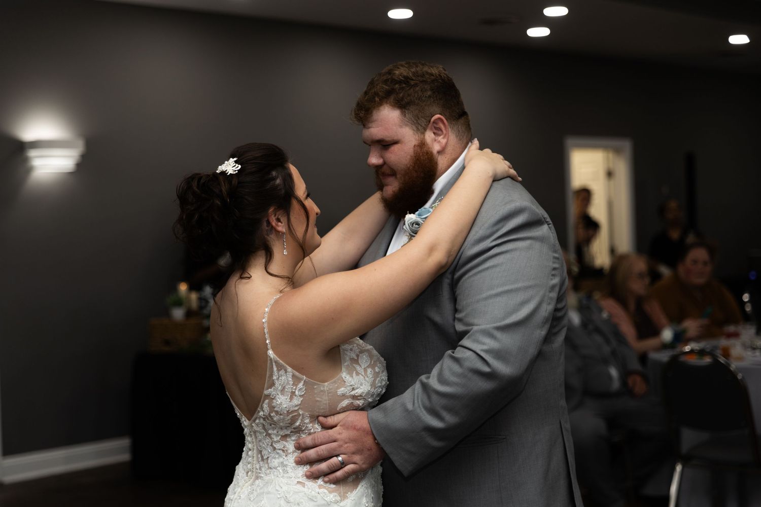 A couple shares their first dance together at a wedding reception in a dimly lit room.
