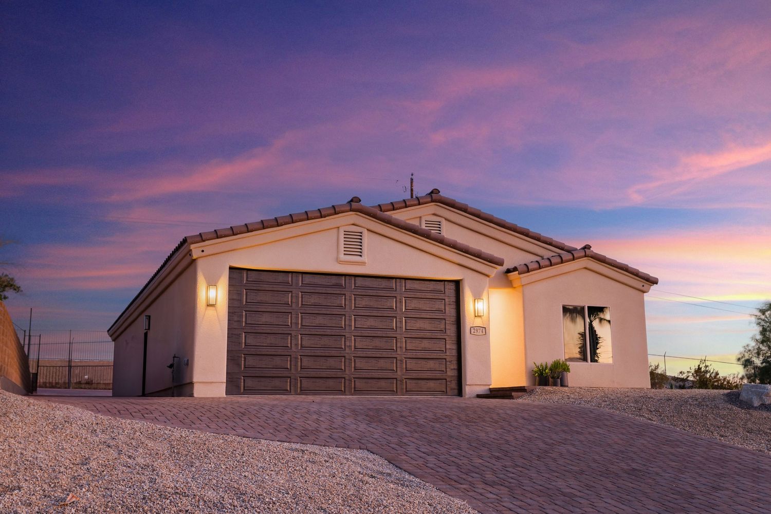 Modern desert home with brown garage door and tan exterior illuminated at sunset with vibrant purple sky.