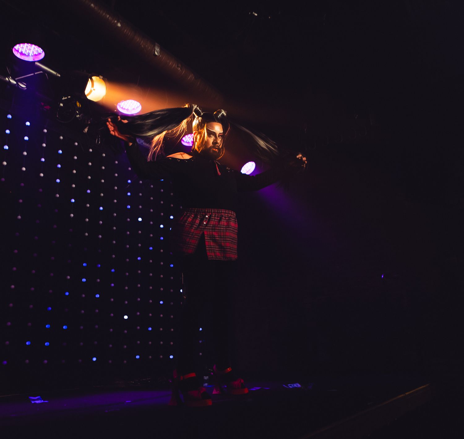 Stage lighting equipment and spotlights illuminate a dark performance space with purple and blue ambient lights in background.