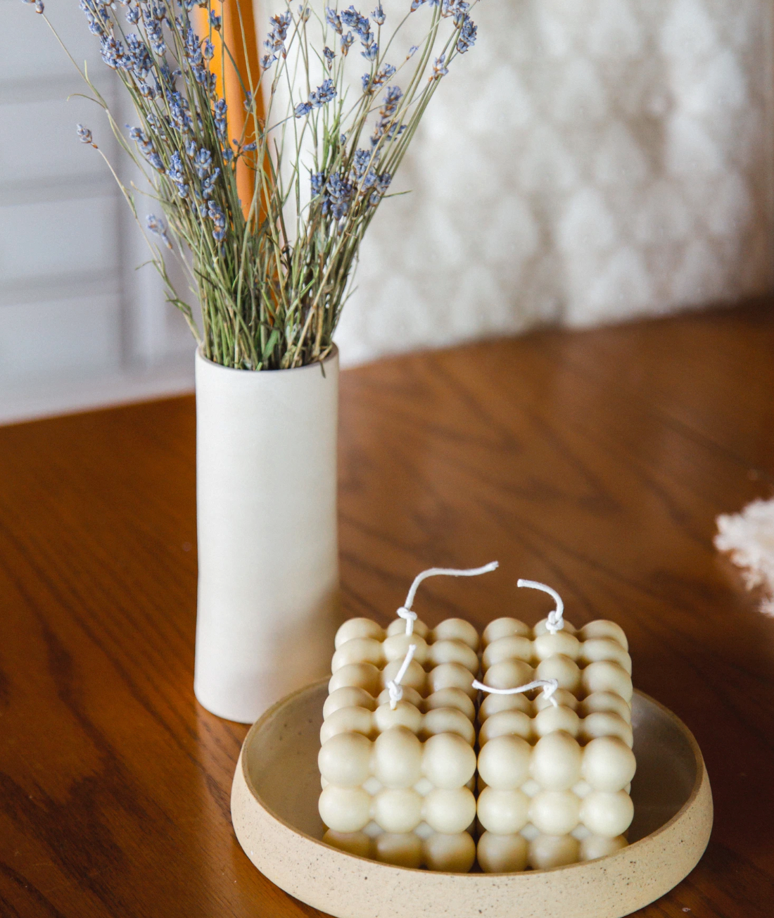 White ceramic vase with dried blue flowers next to decorative bubble candles on wooden surface.
