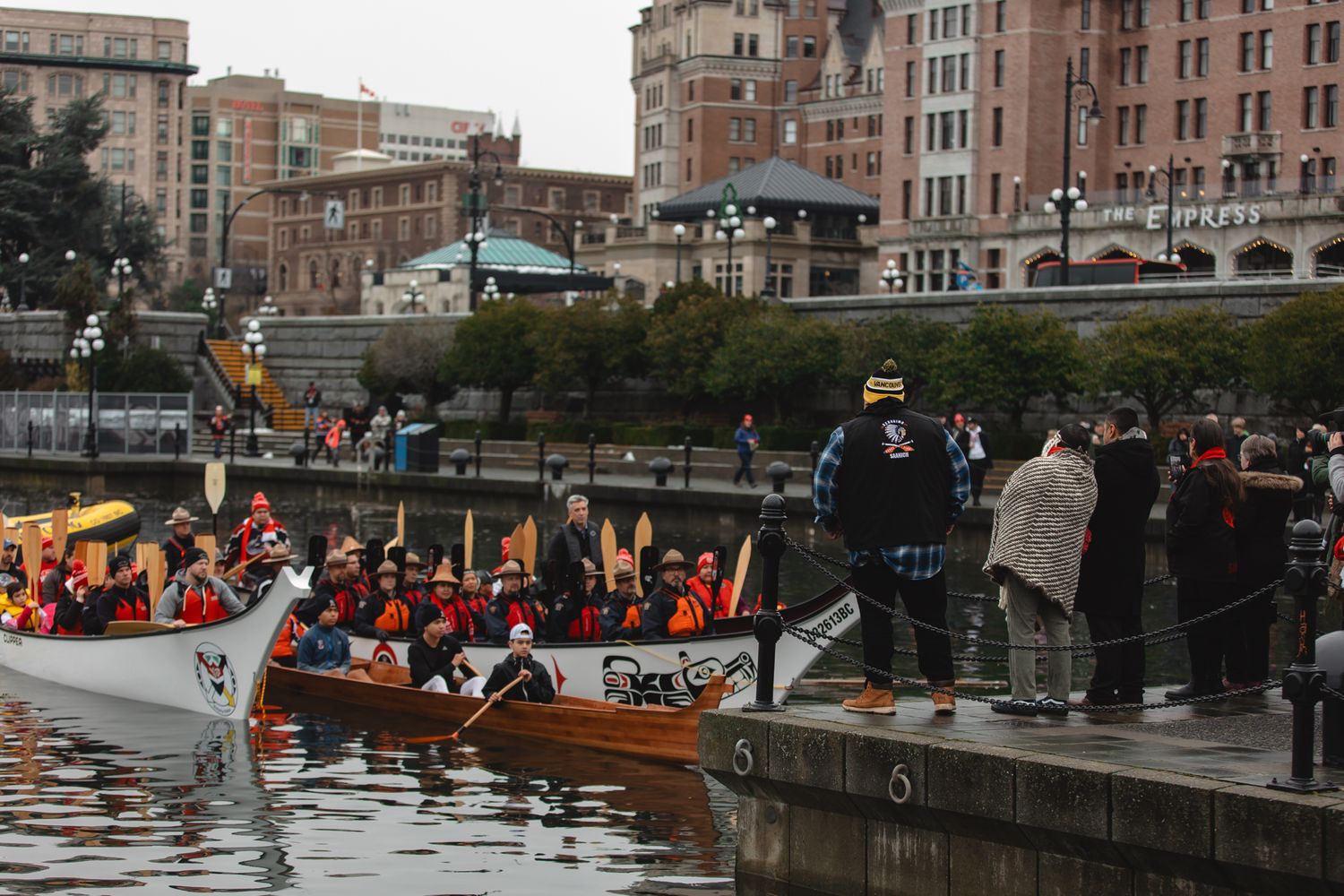 Spectators watch indigenous canoes gather along a waterfront during a cultural celebration in Seattle, Washington.