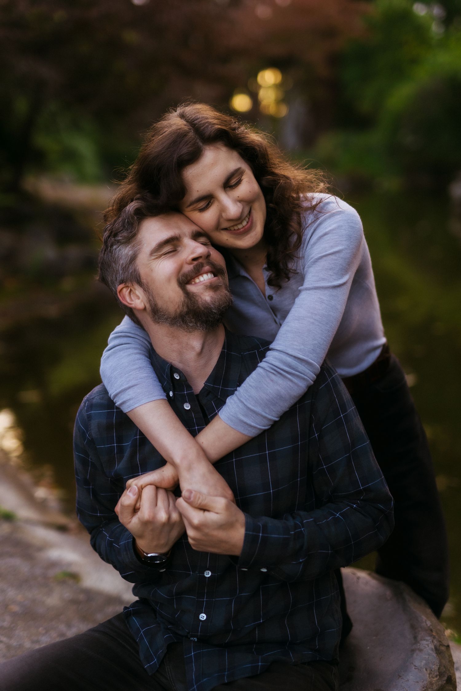 A happy couple embraces and laughs together outdoors during a warm sunset photoshoot in nature.