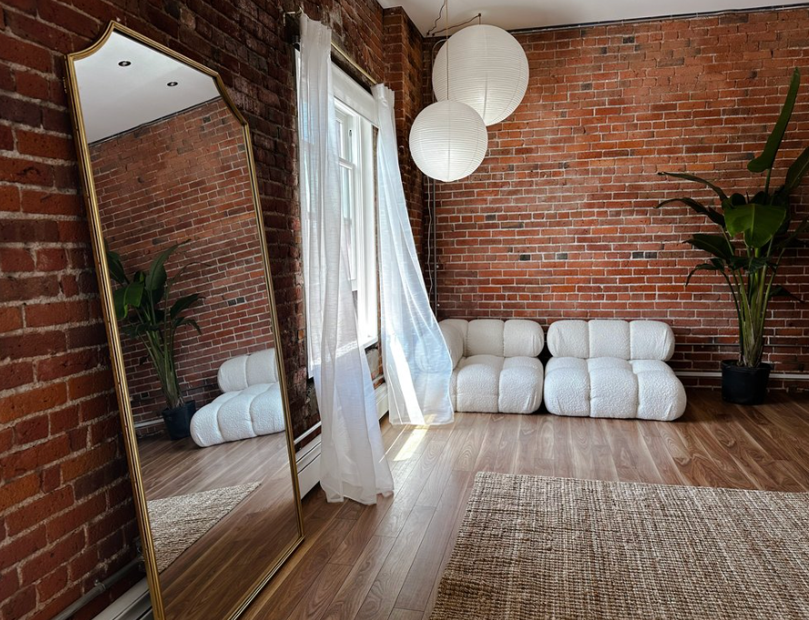 Minimalist studio space with brick walls, floor mirror, white cushions and paper lanterns.
