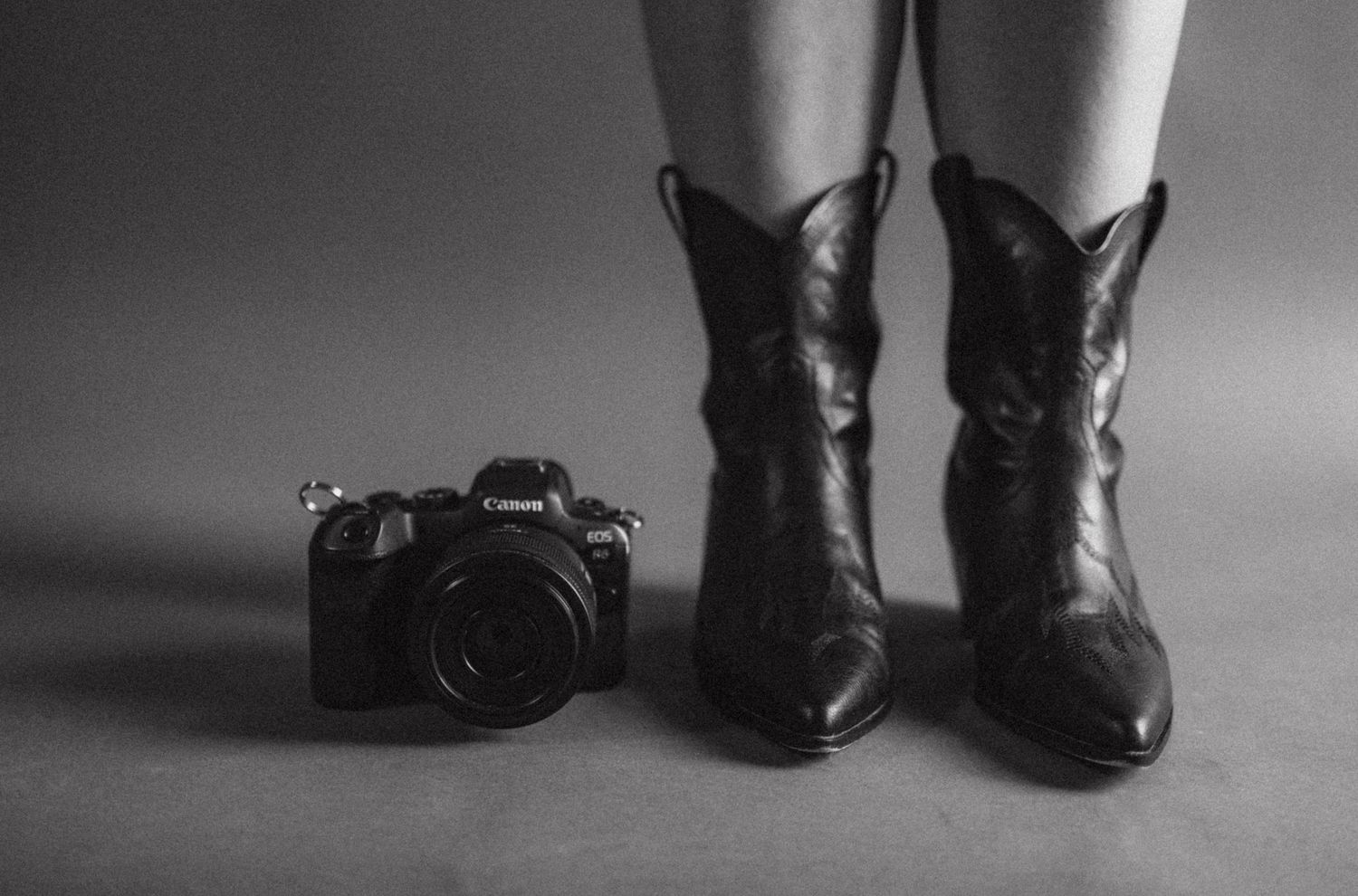 Black cowboy boots and vintage camera on gray background in artistic black and white composition.