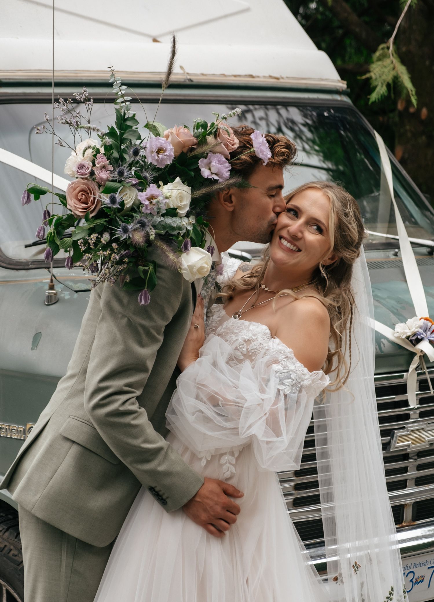 A romantic wedding moment by a boat with a lace dress, floral crown, and sage green suit.