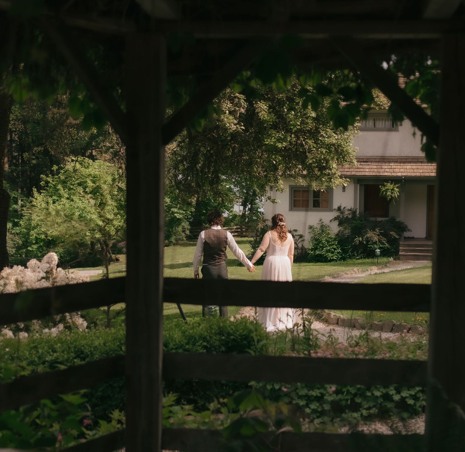 A romantic garden wedding scene viewed through a wooden pergola frame.