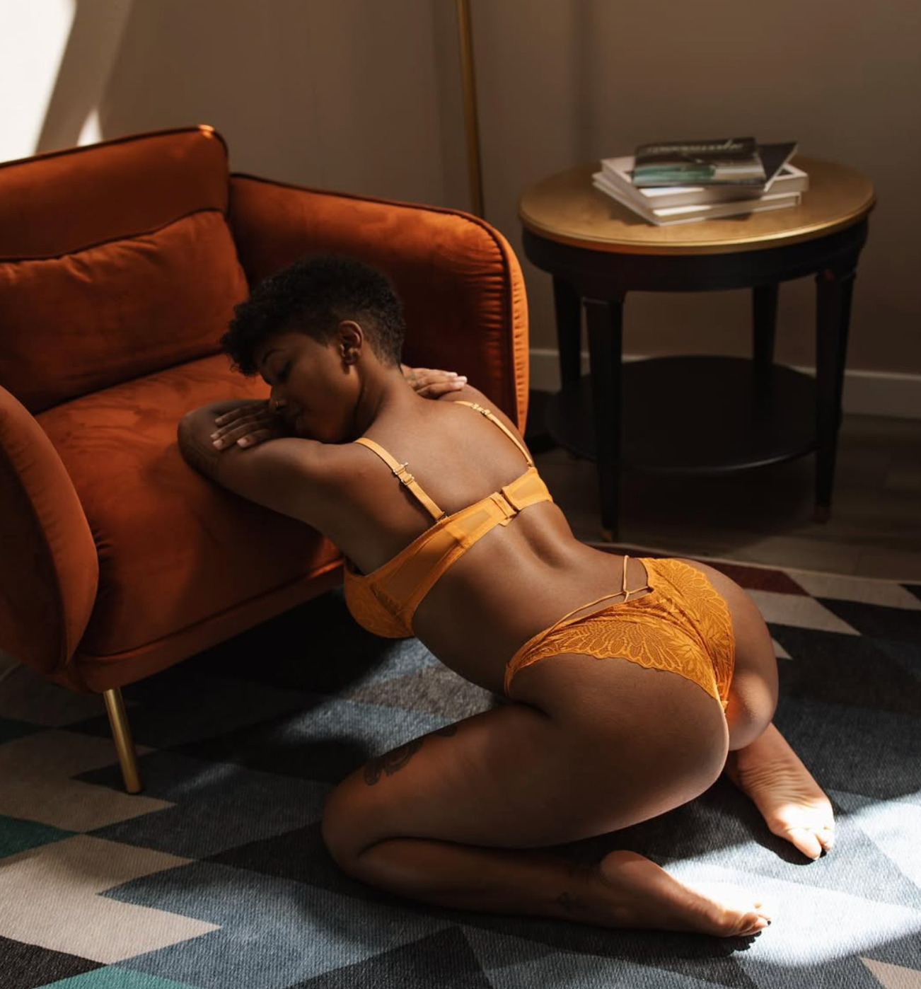 Artistic pose on checkered floor against orange couch in warm lighting.