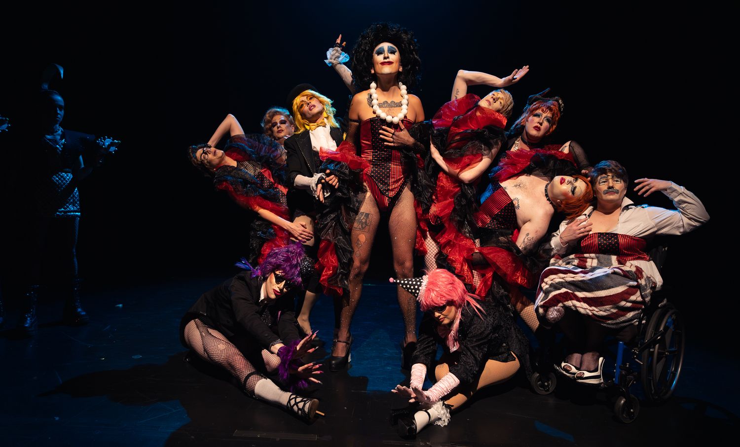 A dramatic burlesque performance features dancers in black and red costumes striking dynamic poses on a dark stage.