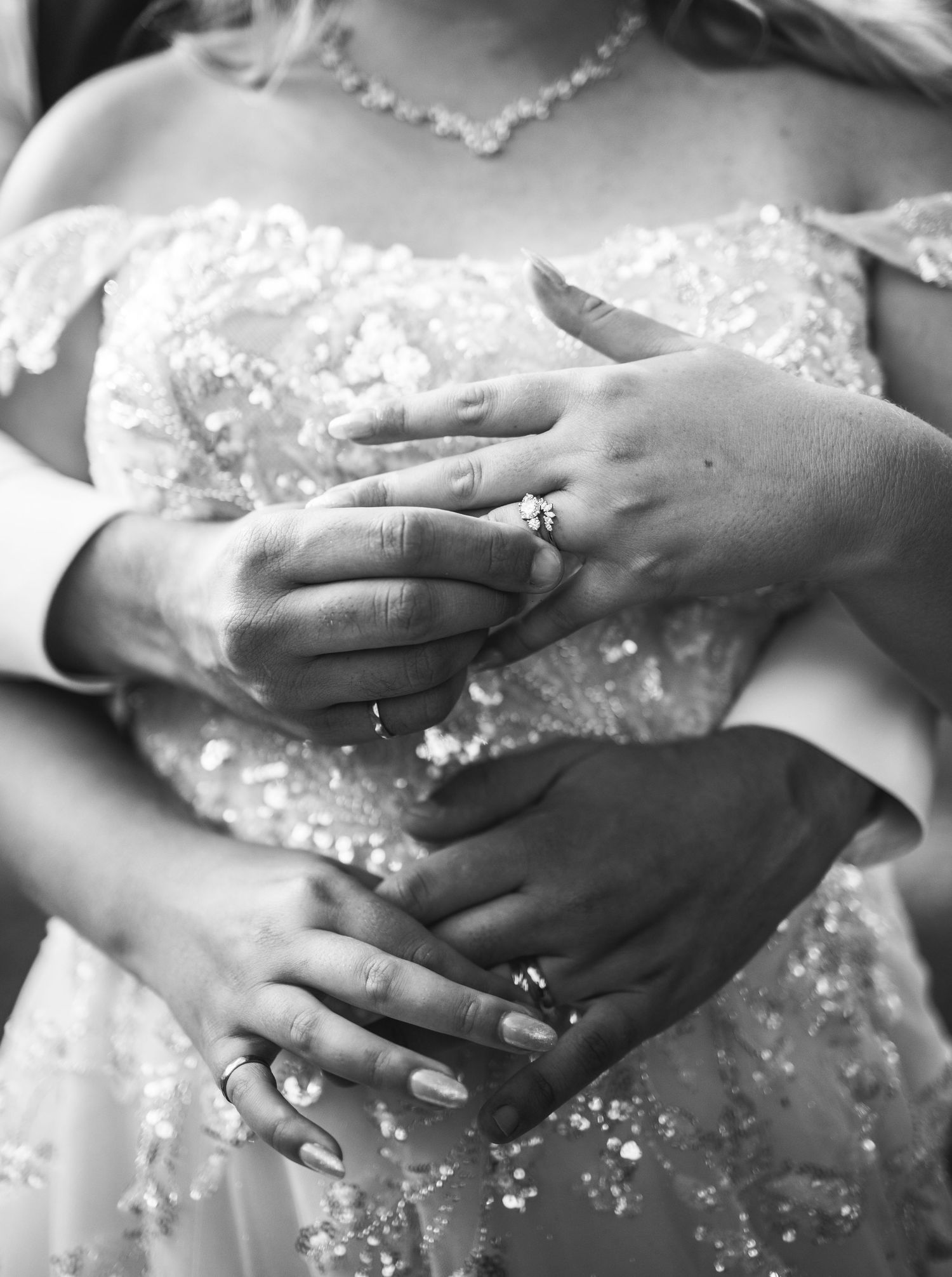 Close-up of hands showing wedding rings and lace details on a bridal gown.