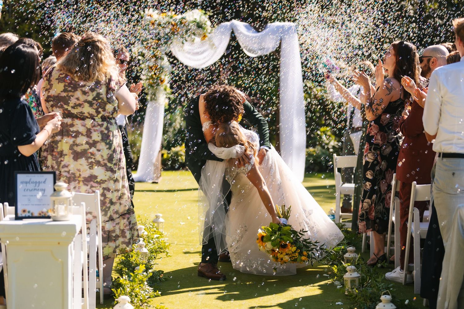 Guests shower confetti over the newlyweds during an outdoor garden ceremony celebration.