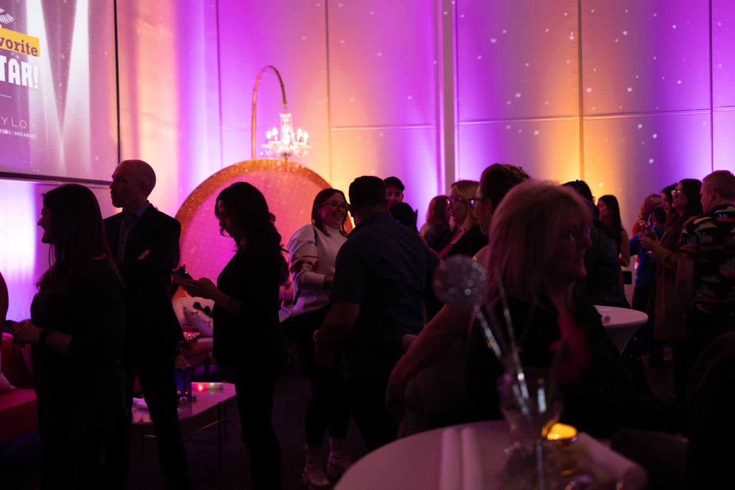Silhouettes of party guests mingling in a dark room with purple and orange mood lighting and glowing ambiance.