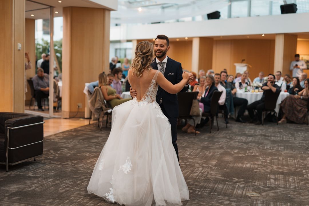 A couple performs their first dance in an elegant ballroom surrounded by wedding guests.