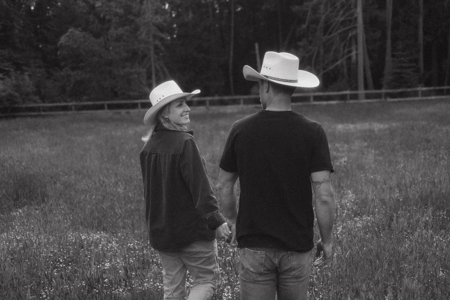 Two people wearing cowboy hats stand together in a field with trees in black and white photography.