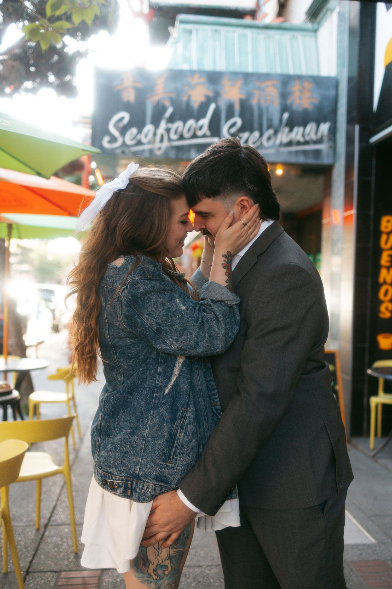 A romantic couple embraces outside a seafood restaurant on a street with Chinese signage and yellow chairs.