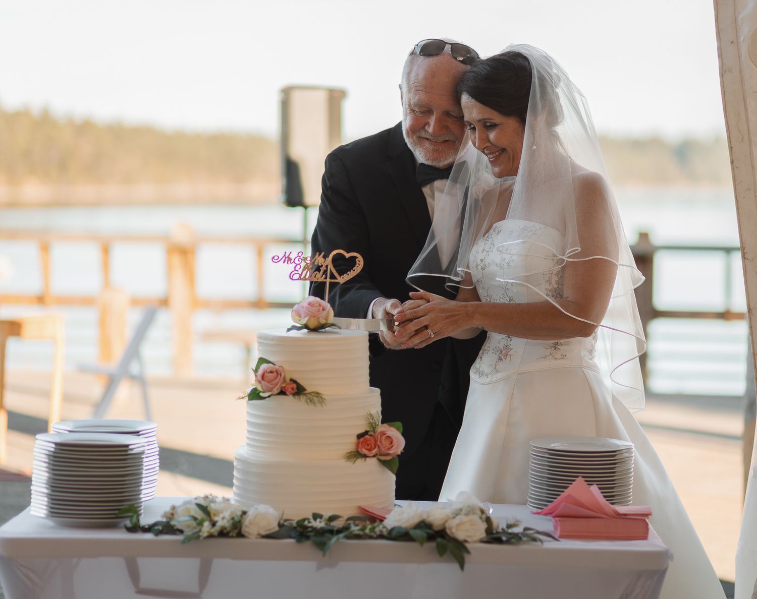 A couple cuts their elegant white wedding cake together at their waterfront reception.