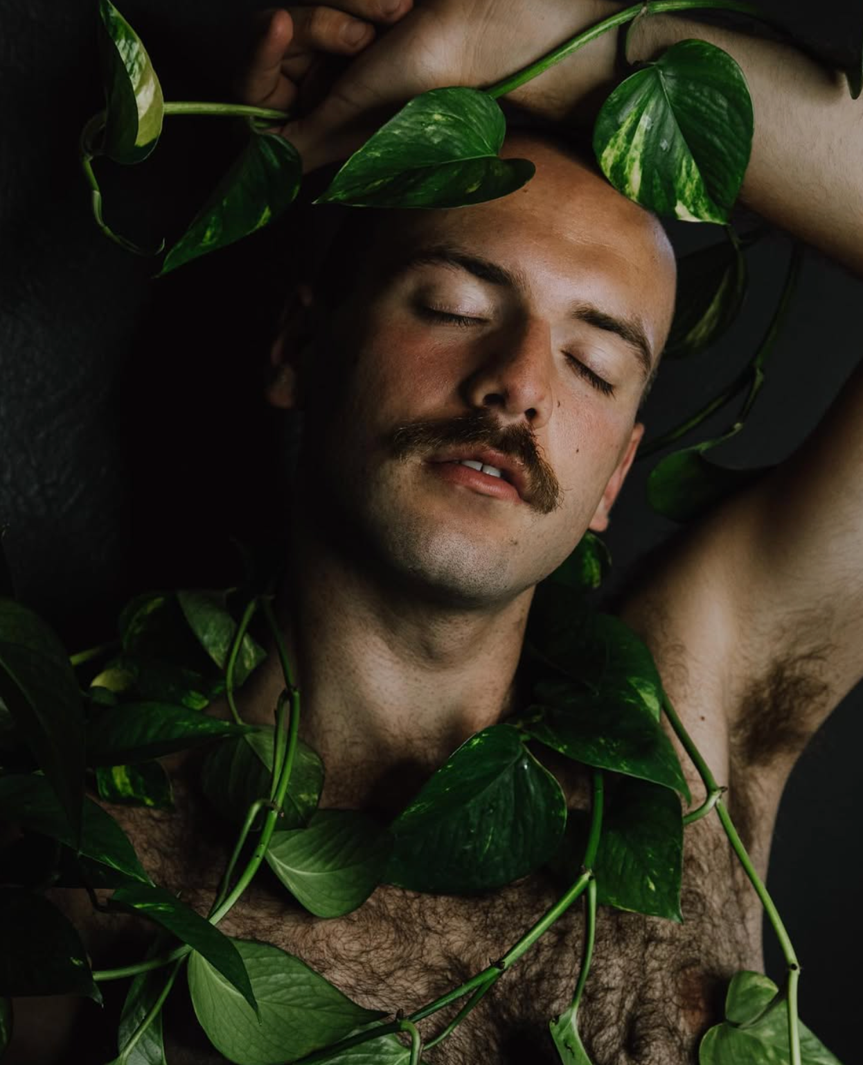 Artistic portrait with green leaves adorning subject in dramatic lighting.