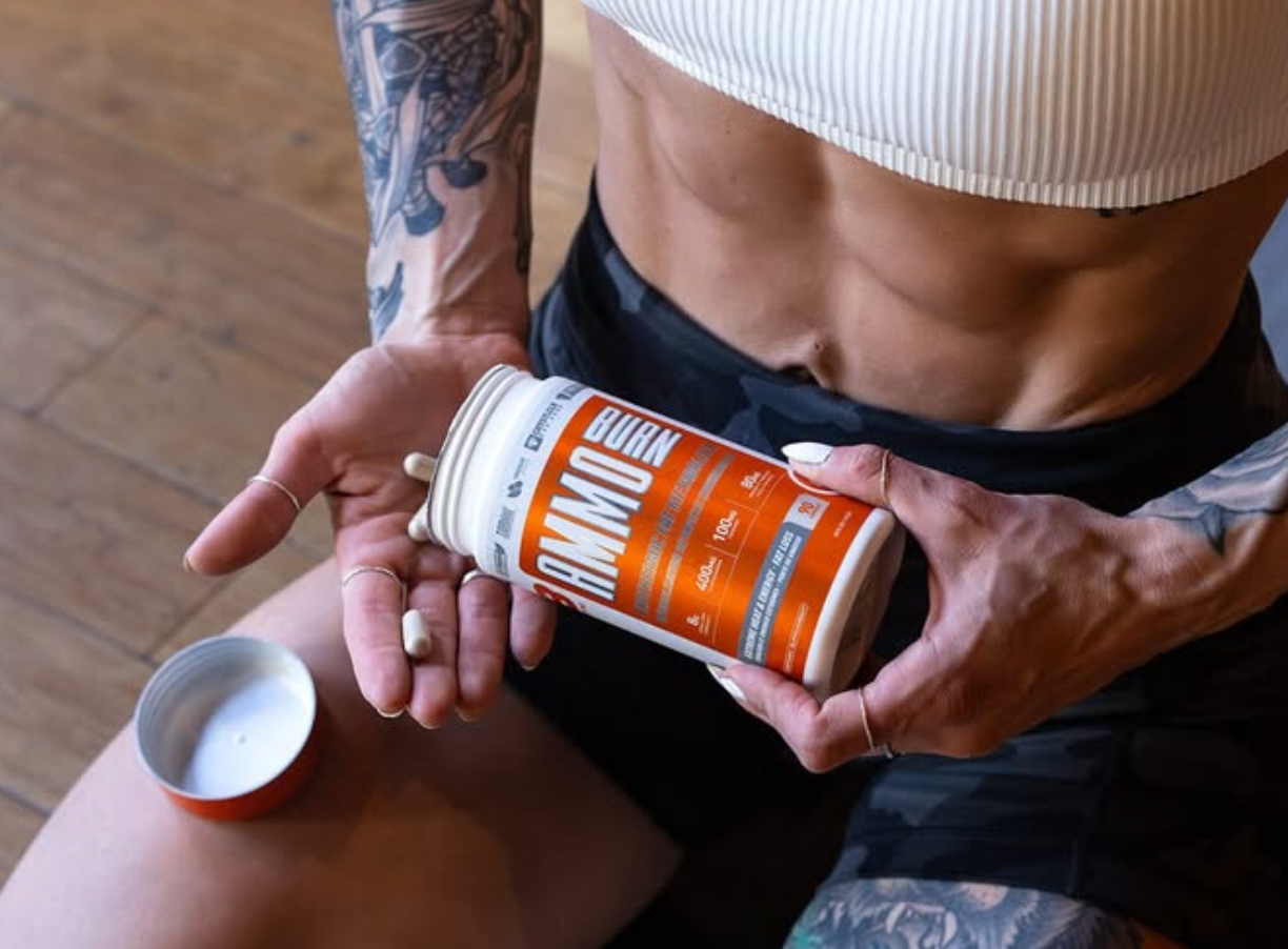 Tattooed hands hold an orange supplement bottle against athletic wear.