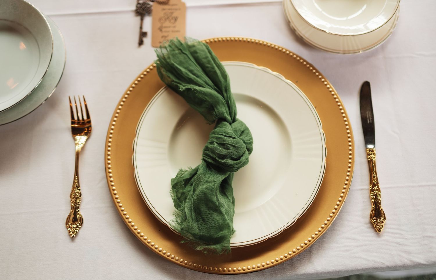An elegant place setting features a green napkin artfully arranged on a gold-rimmed plate with golden cutlery.