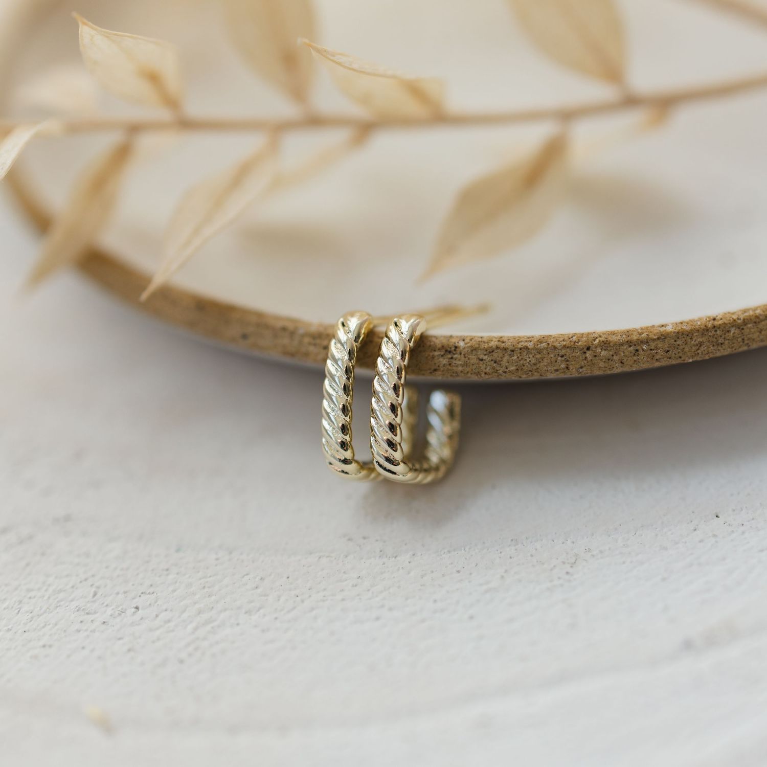 Gold twisted rope style ring displayed on beige leather surface.