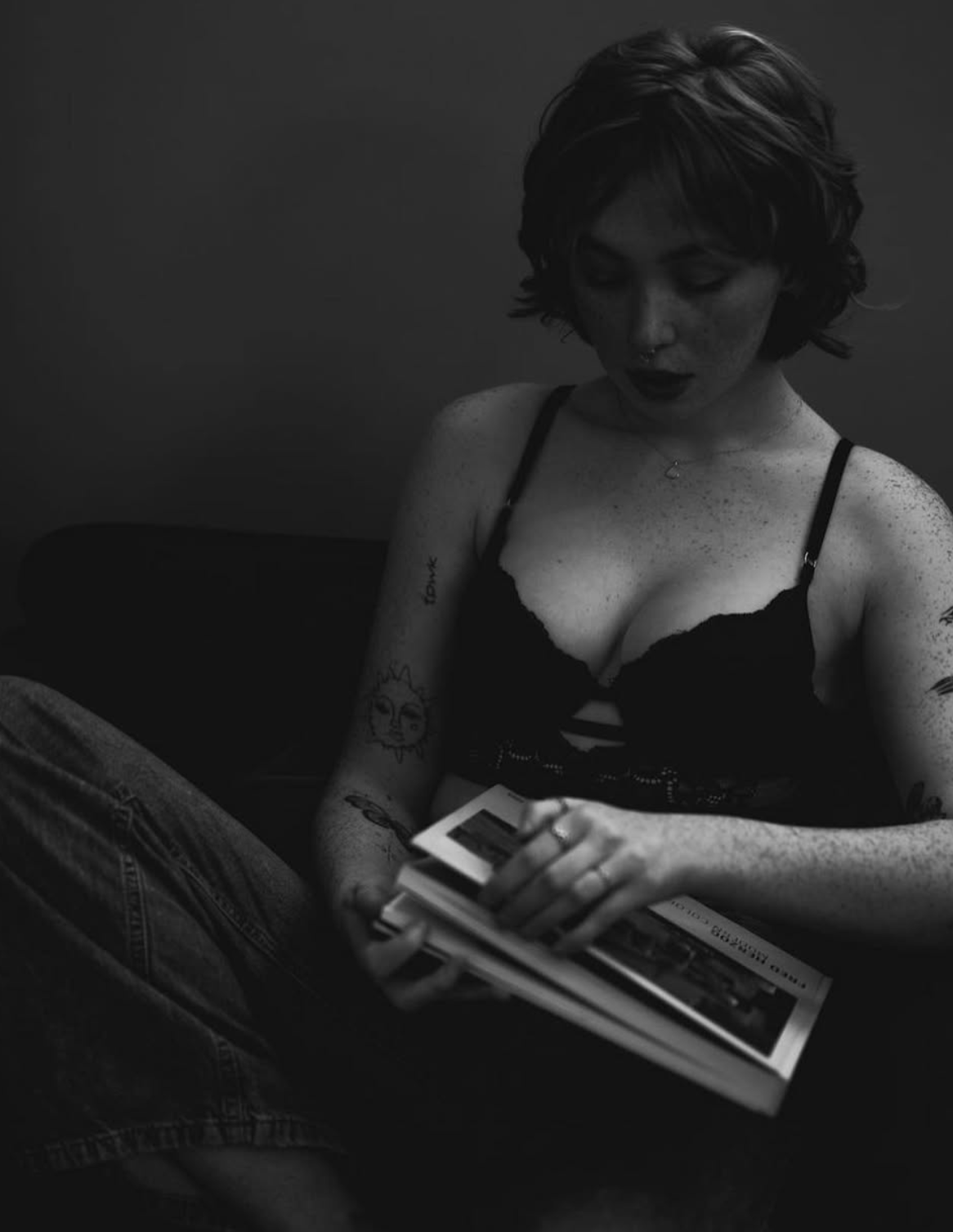 Moody black and white portrait of person reading book while wearing dark lingerie.