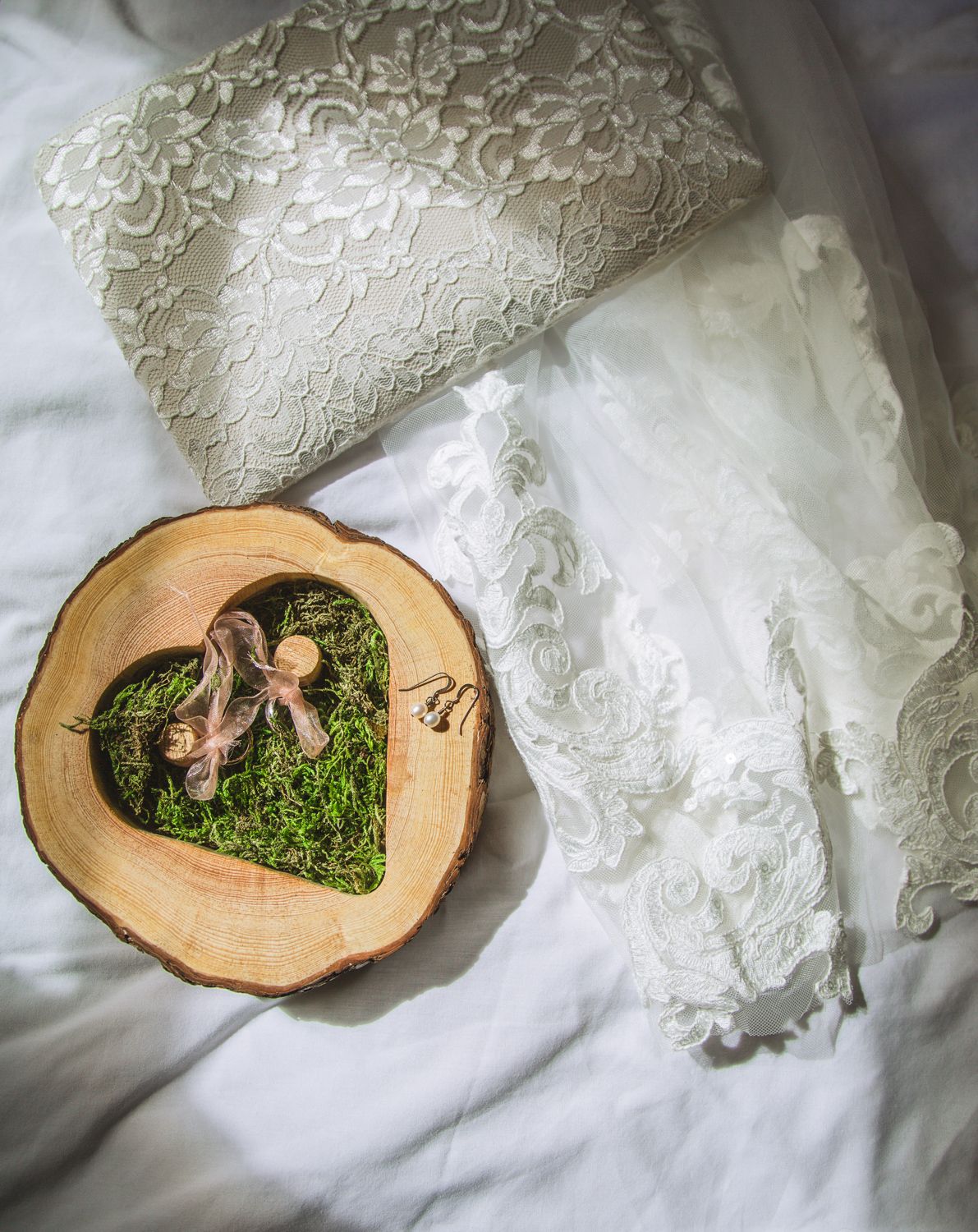 Rustic wood slice with moss heart and lace fabric pieces featuring intricate patterns in wedding decor.