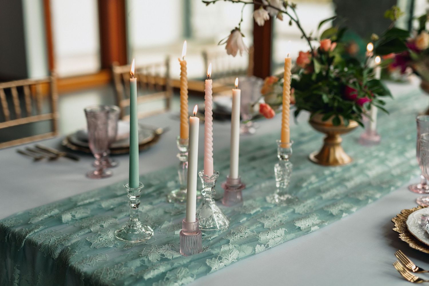 An elegant table setting with taper candles and floral centerpieces on mint green tablecloth.