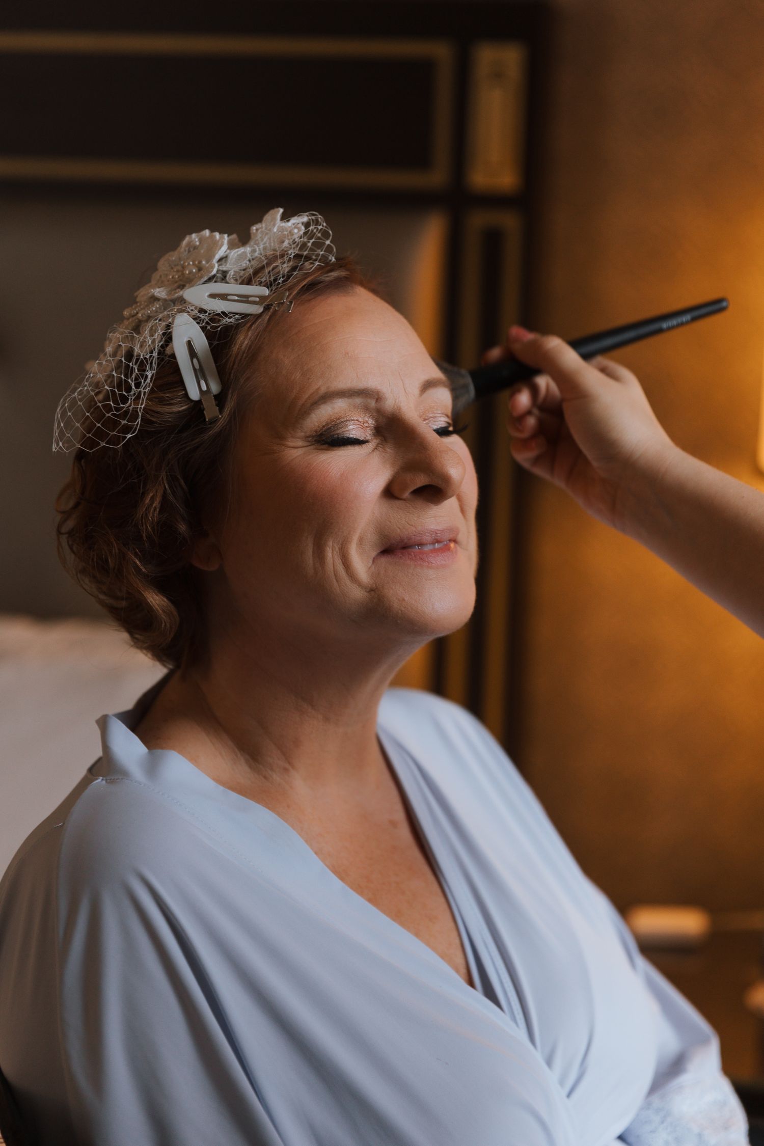A person getting their makeup professionally applied while wearing a white robe and delicate hair accessory.